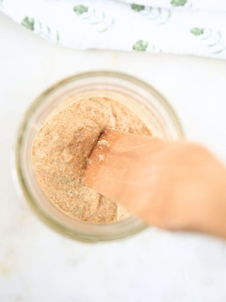A jar of sourdough starter with a spurtle in it