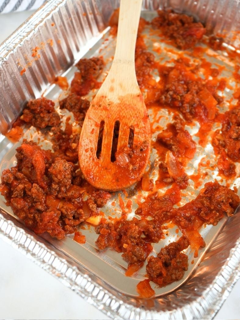 A foil pan with a layer of meat sauce on the bottom