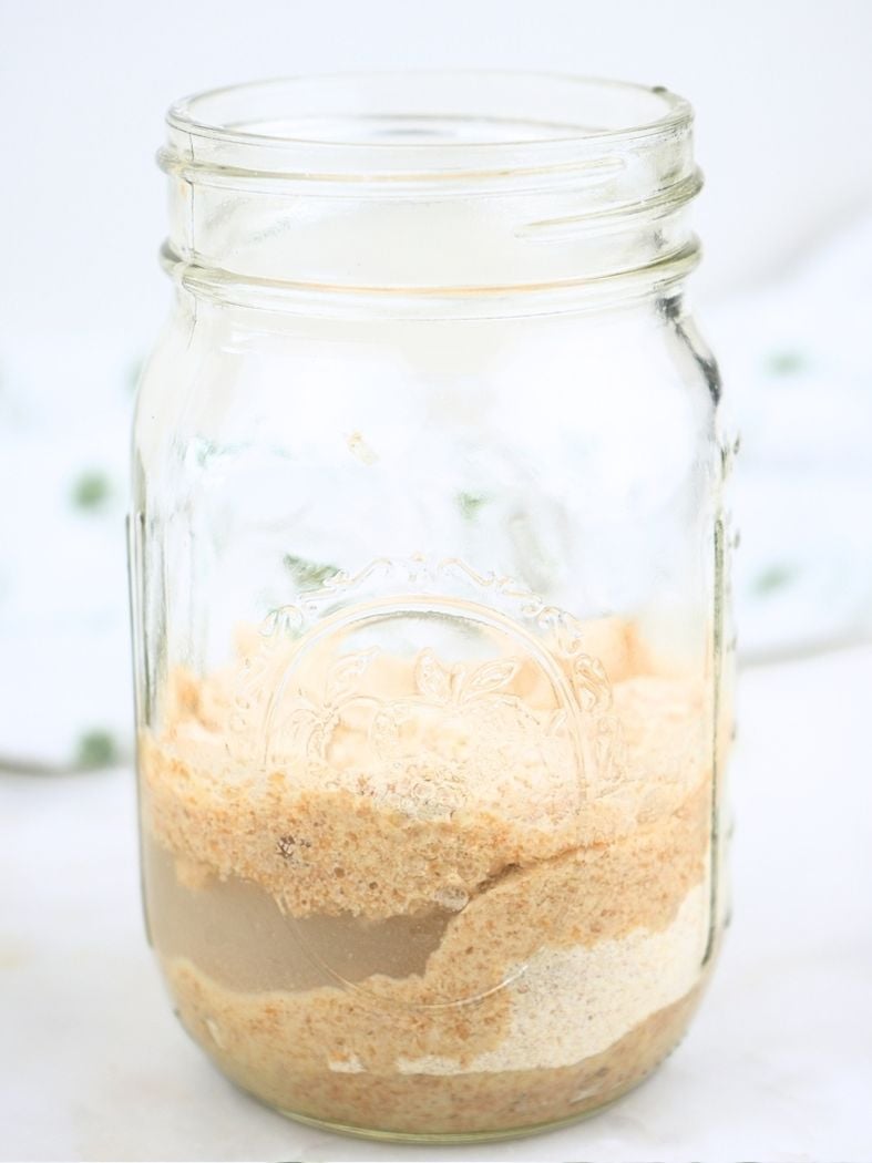 A jar of starter, showing the layers of starter, flour, and water before stirring