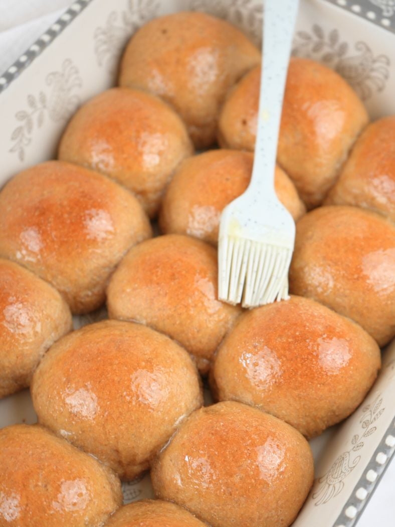 Fresh-milled dinner rolls brush with melted butter, shown with a silicone pastry brush