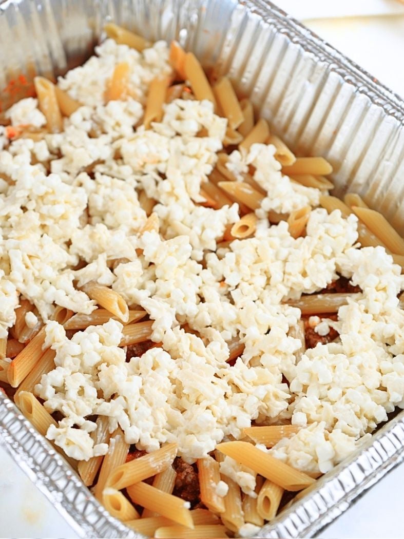 A layer of sauce, noodles, and cheese in a aluminum pan