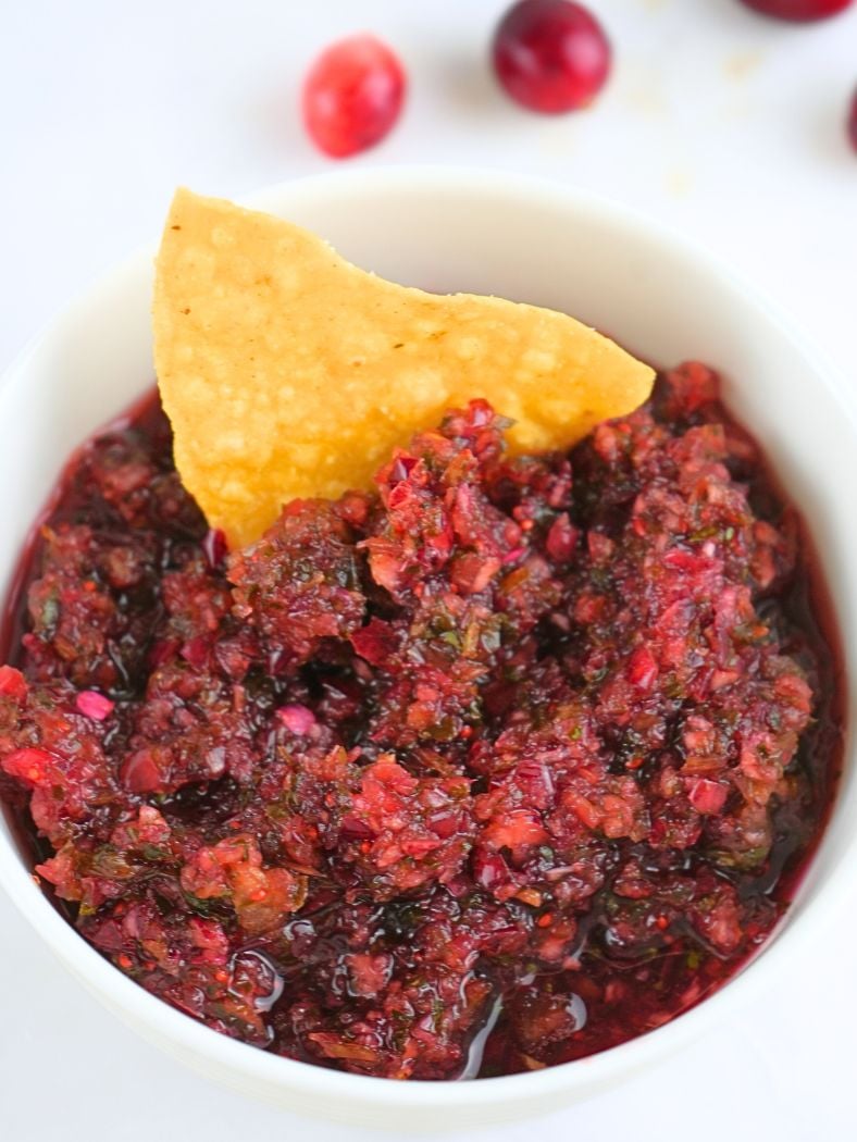 A bowl of cranberry salsa with a tortilla chip in it