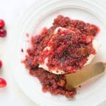 A block of cream cheese covered in cranberry salsa with fresh cranberries scattered