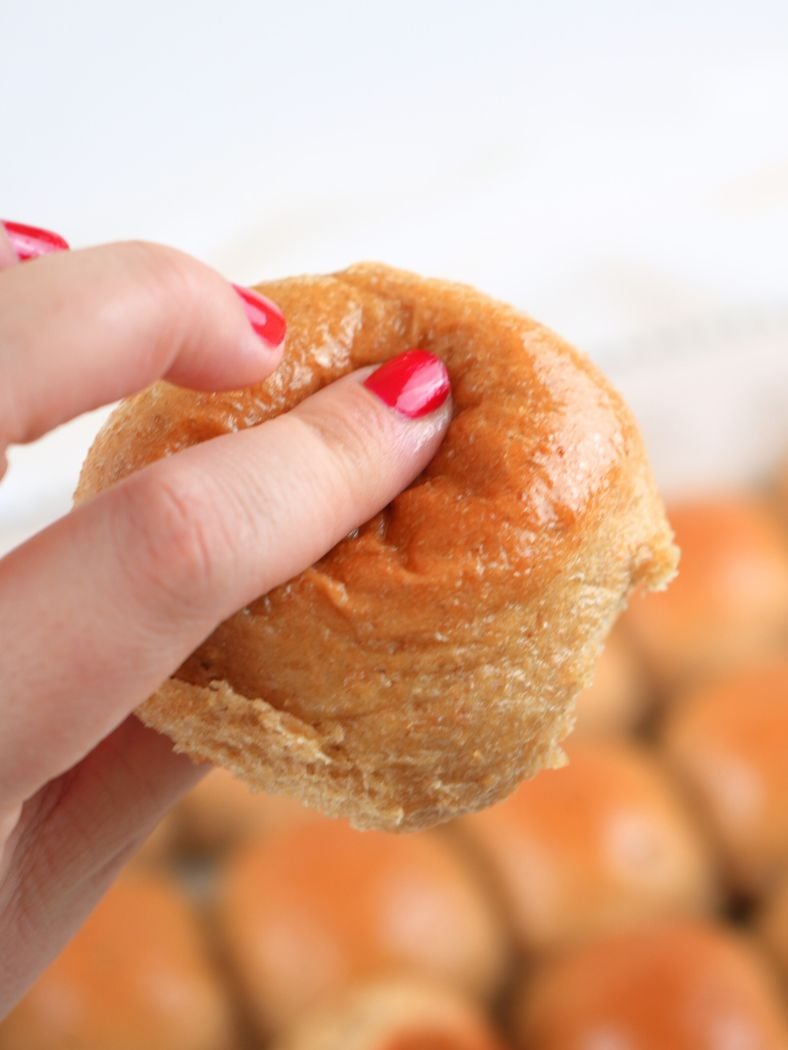 A hand squeezing a fresh-milled dinner roll, showing how soft it is