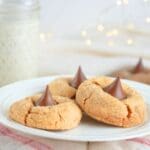 A plate of three sourdough peanut butter blossoms with twinkle lights and a jar of milk in the background