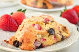 A strawberry chocolate chip sourdough scone on a plate with fresh berries scattered in the background
