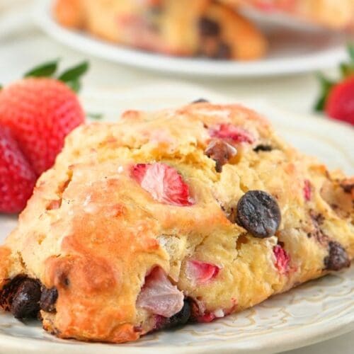 A strawberry chocolate chip sourdough scone on a plate with fresh berries scattered in the background