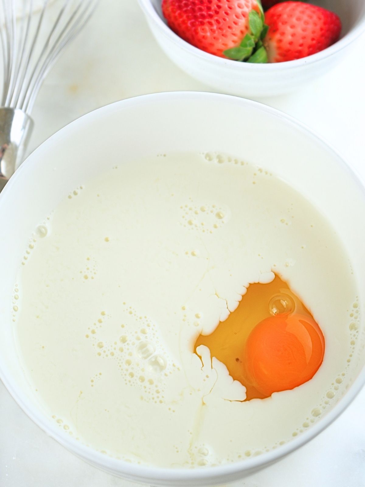 Milk and a whole egg in a white bowl.