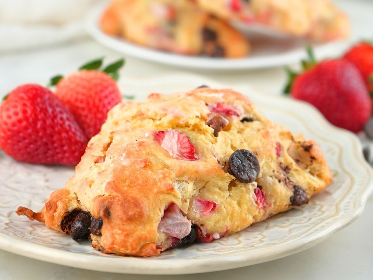 A strawberry chocolate chip sourdough scone on a plate with fresh berries scattered in the background.