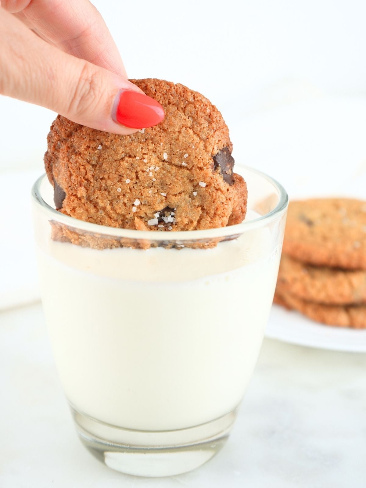 A fresh-milled chocolate chip cookie being dunked in a glass of milk.