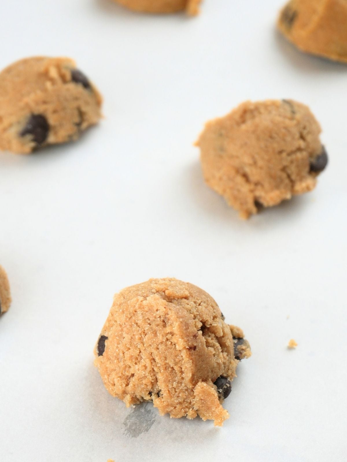 Scoops of chocolate chip cookie dough on a baking sheet.