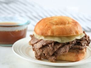 A slow cooker French dip sandwich and a bowl of au jus.