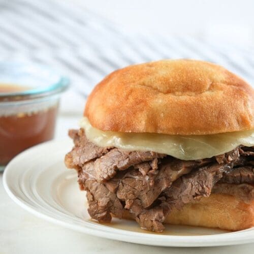 A slow cooker French dip sandwich and a bowl of au jus.
