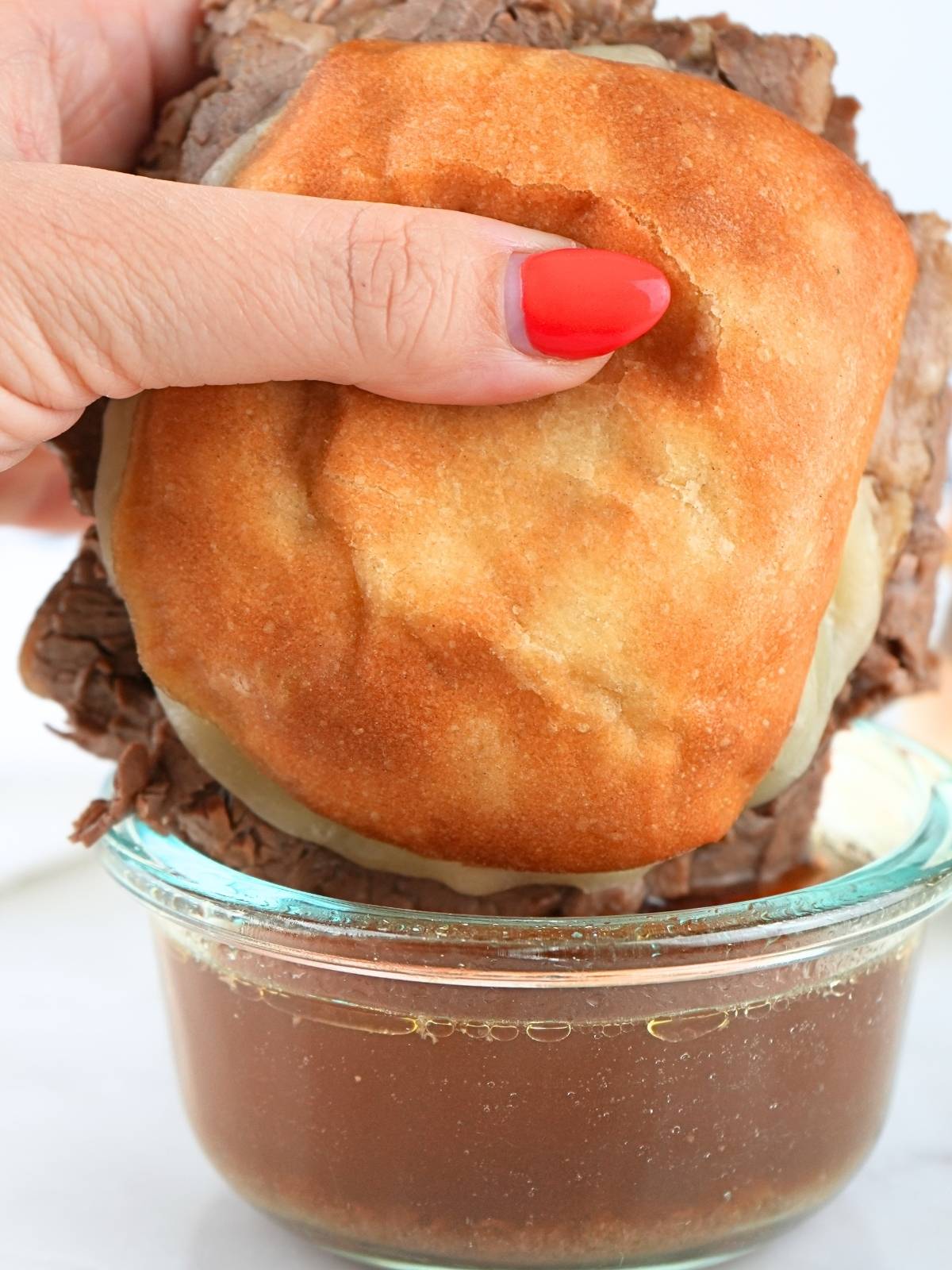 A hand dipping a French dip in a bowl of au jus.
