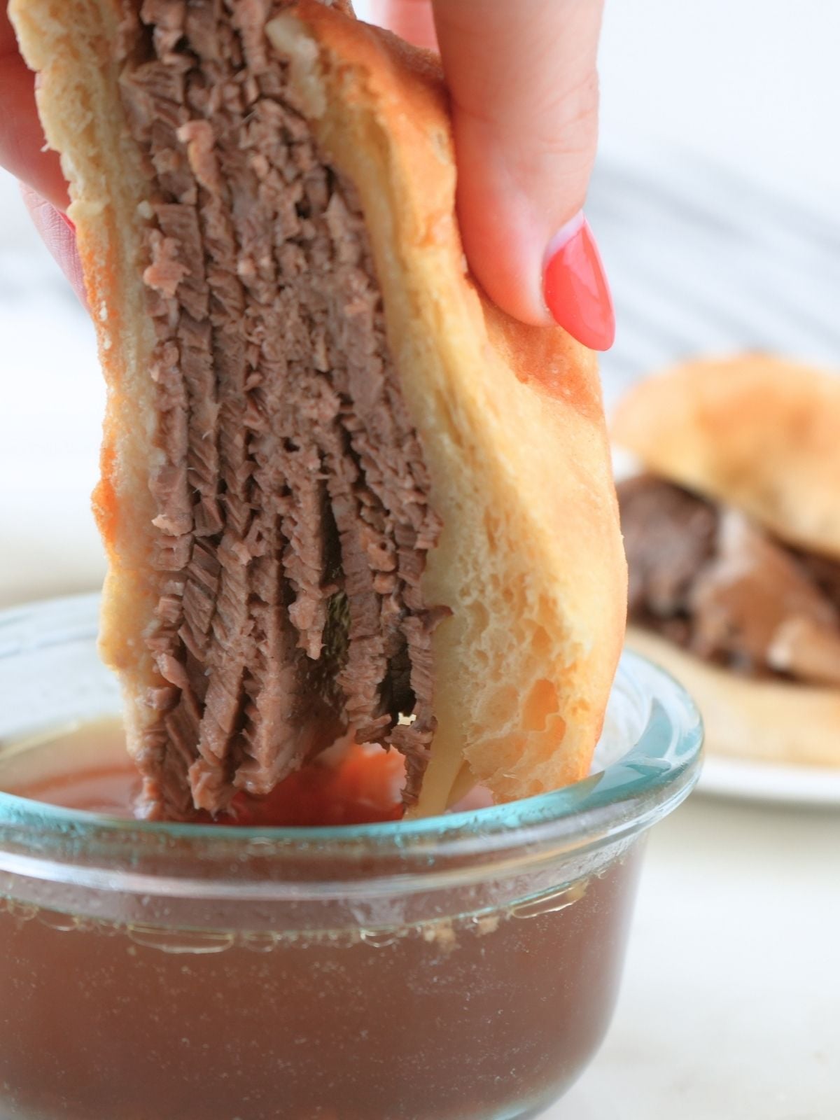 A French dip sandwich being dipped into a bowl of au jus.