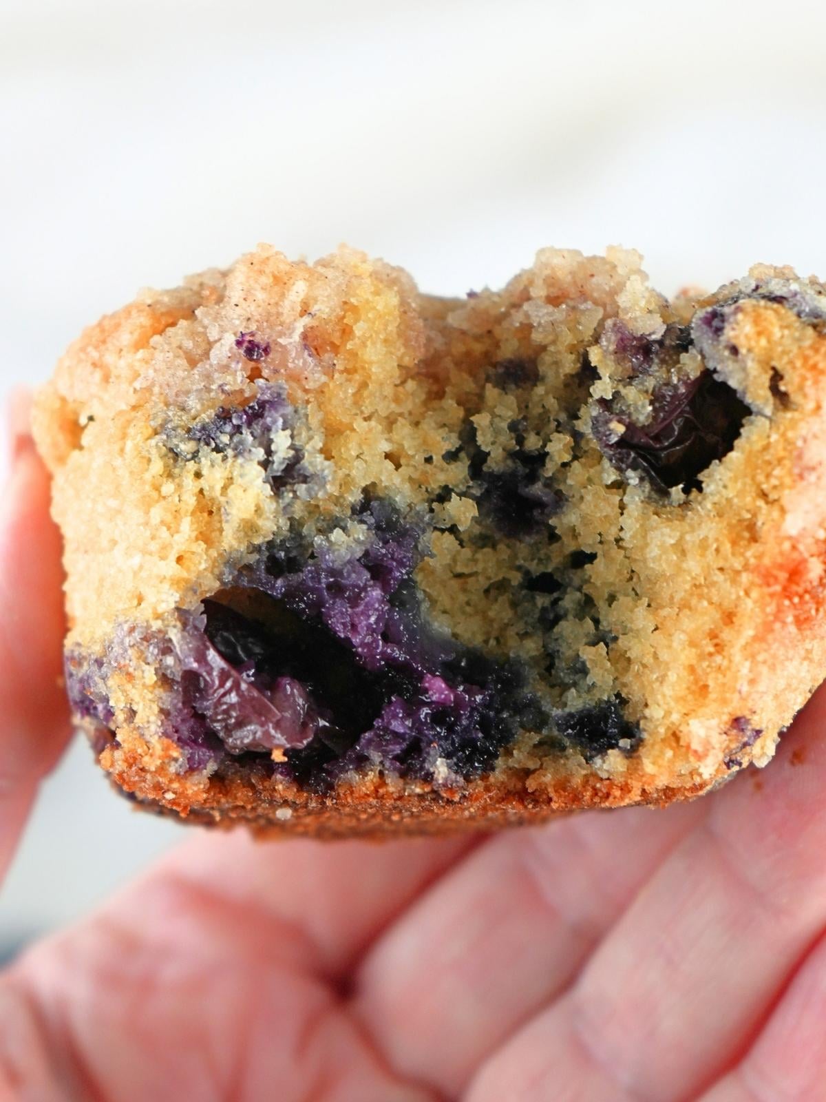 A hand holding a muffin with a bite taken out of it.