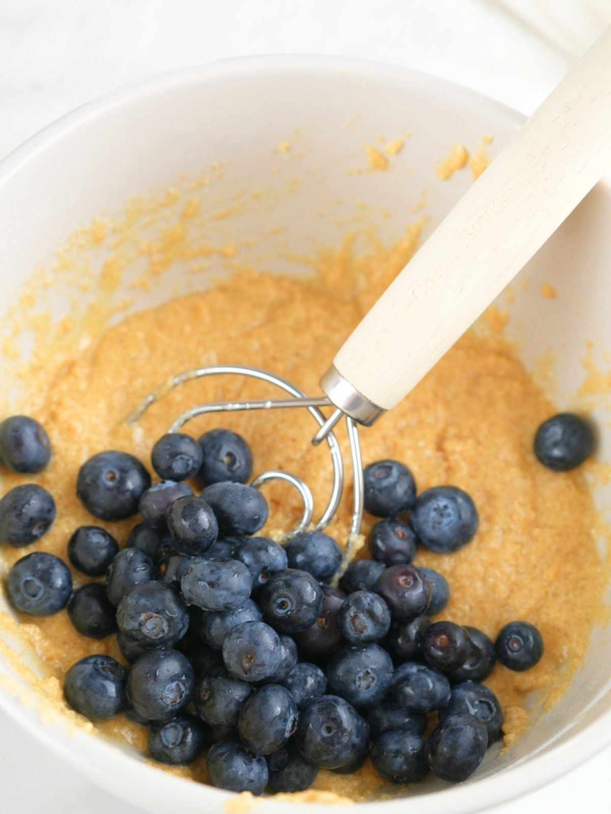 Fresh blueberries on top of fresh-milled muffin batter in a mixing bowl.