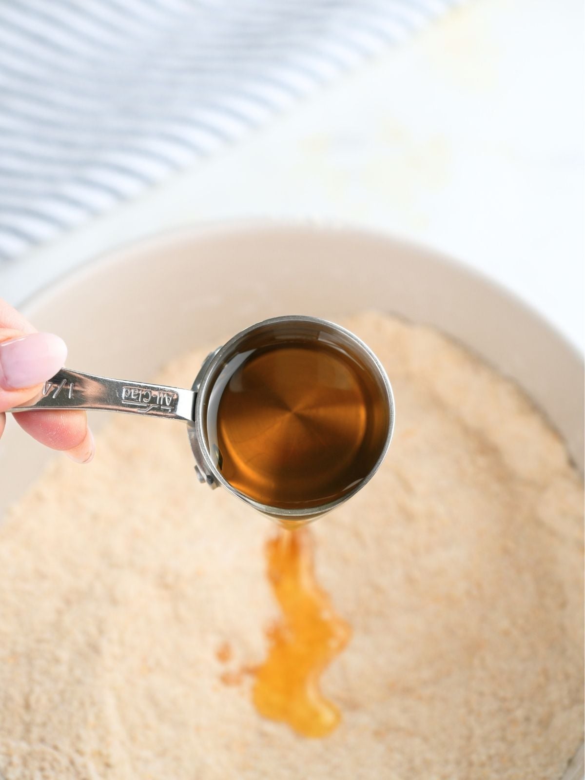 A hand pouring a measuring cup of avocado oil into dry ingredients.
