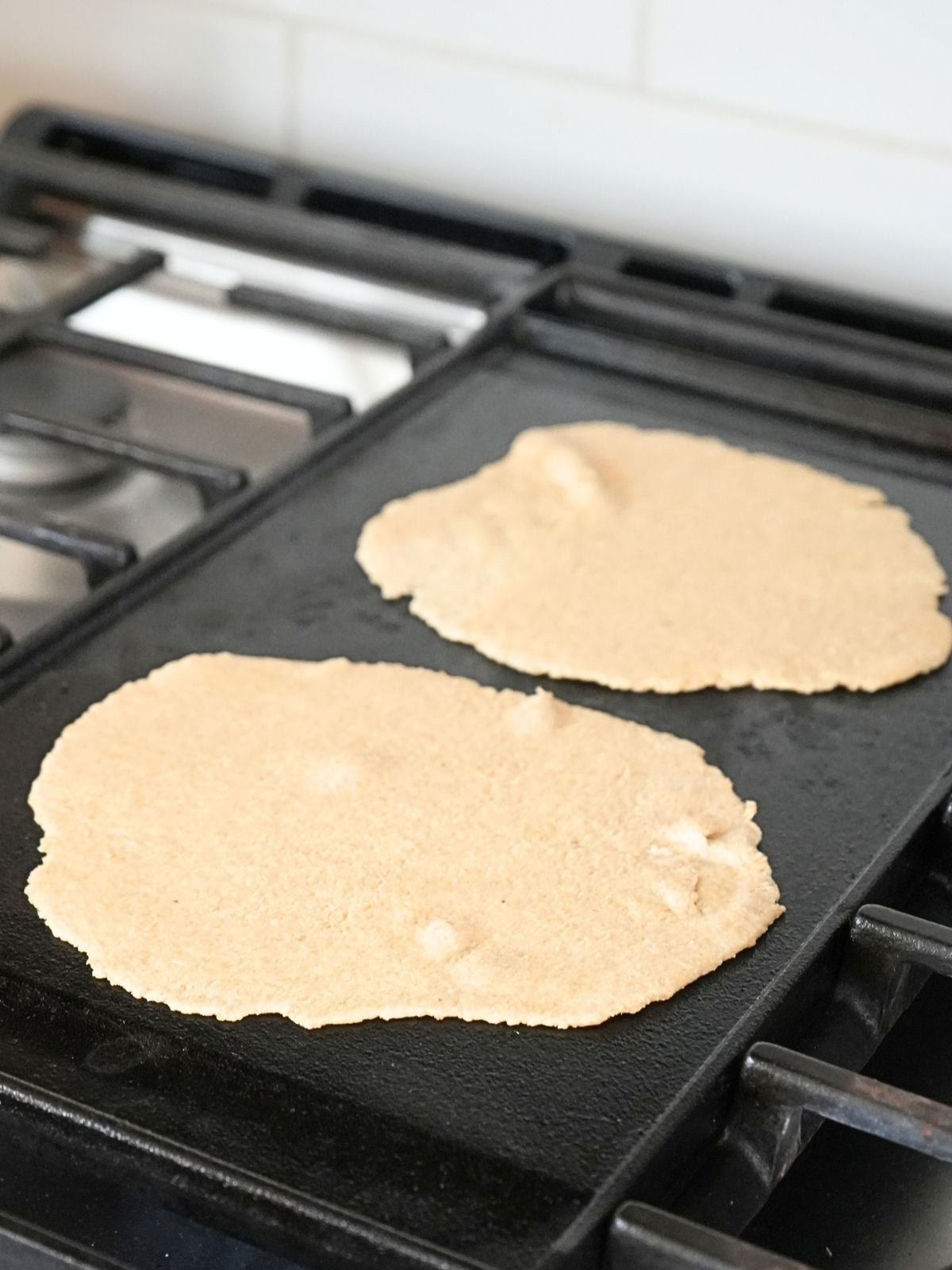 Two fresh-milled tortillas cooking on a cast iron griddle.