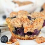 A blueberry muffin with fresh flour on a plate with fresh berries.