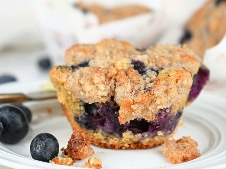 A blueberry muffin with fresh flour on a plate with fresh berries.