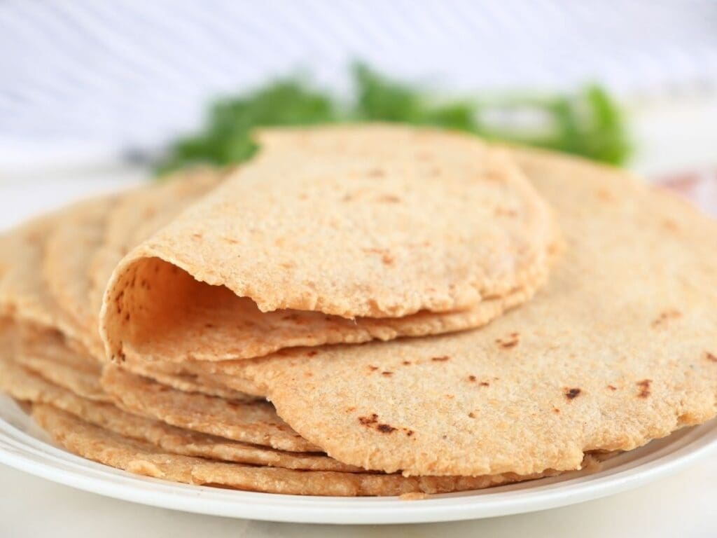 A stack of fresh-milled tortillas on a plate with one on top folded in half.