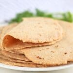 A stack of fresh-milled tortillas on a plate with one on top folded in half.