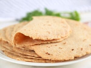 A stack of fresh-milled tortillas on a plate with one on top folded in half.