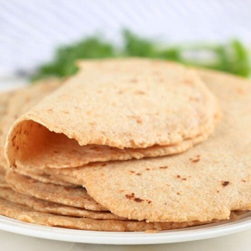 A stack of fresh-milled tortillas on a plate with one on top folded in half.