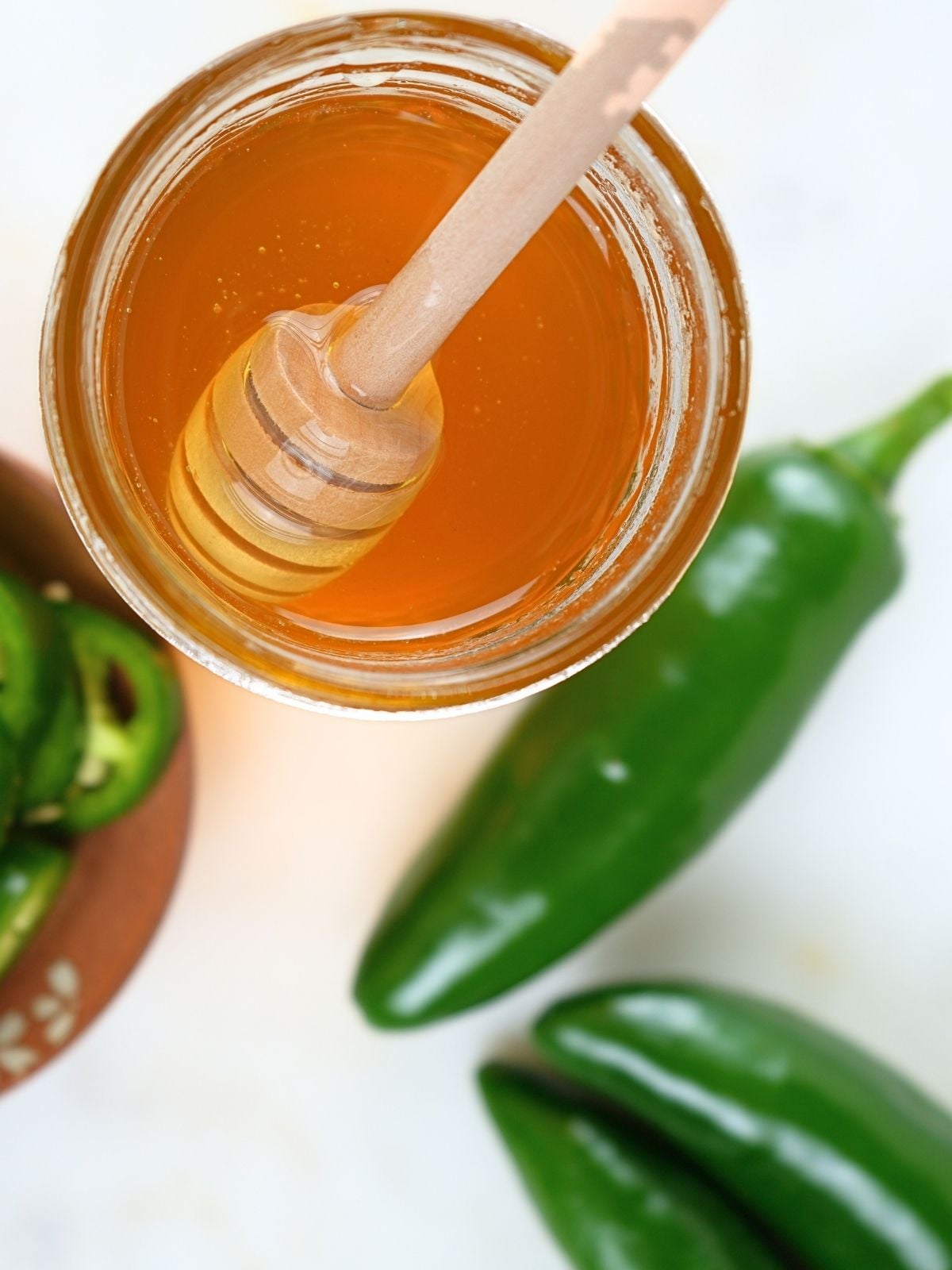 A jar of jalapeño hot honey with a honey stick and peppers.