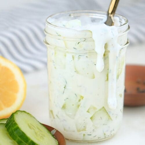 Cucumber ranch dressing in a jar with fresh cucumbers and lemons next to it.