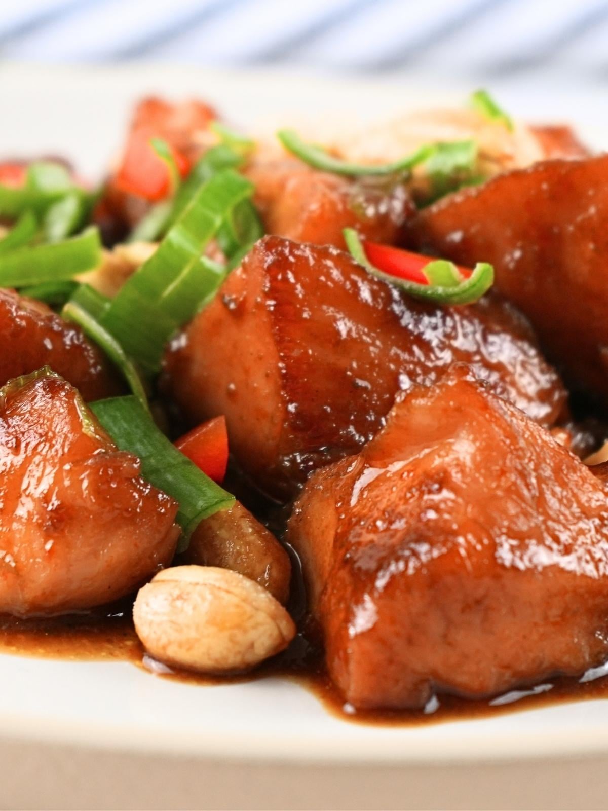 Kung pao chicken on a plate with peanuts and sliced green onions.
