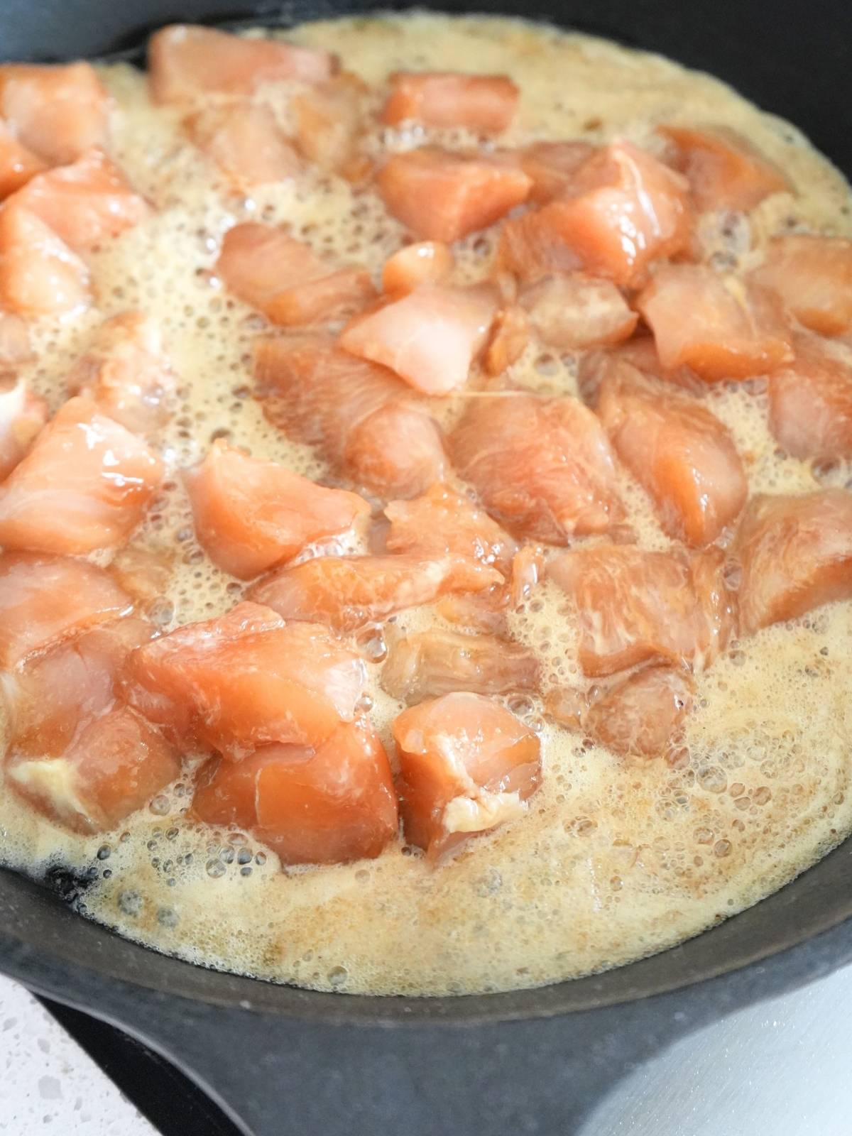 Chicken cooking in a cast iron skillet.