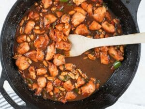 Kung pao chicken in a cast iron skillet next to a decorative towel.