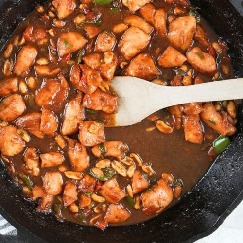 Kung pao chicken in a cast iron skillet next to a decorative towel.