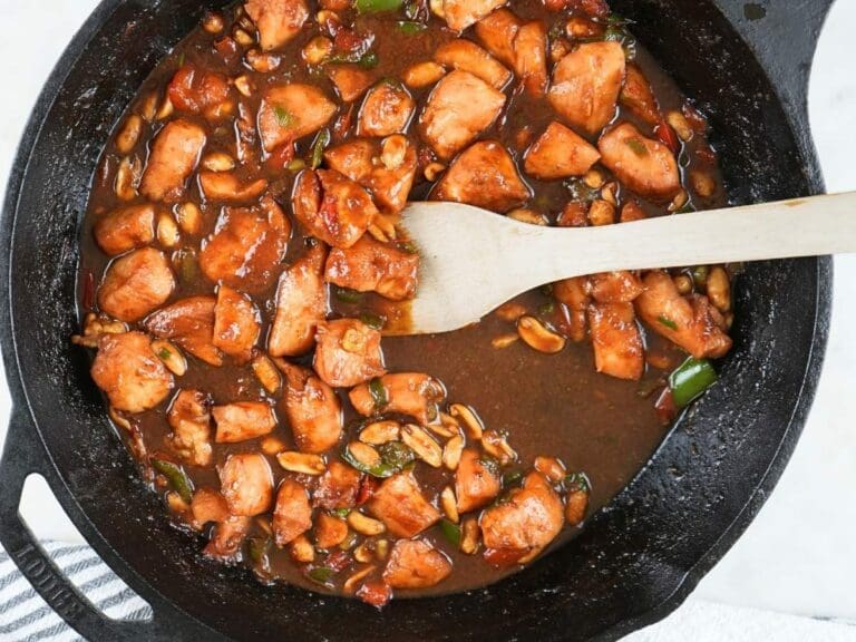Kung pao chicken in a cast iron skillet next to a decorative towel.