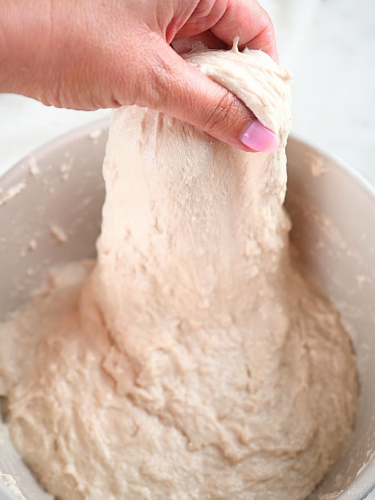 A hand in a bowl of dough showing stretch and folds.