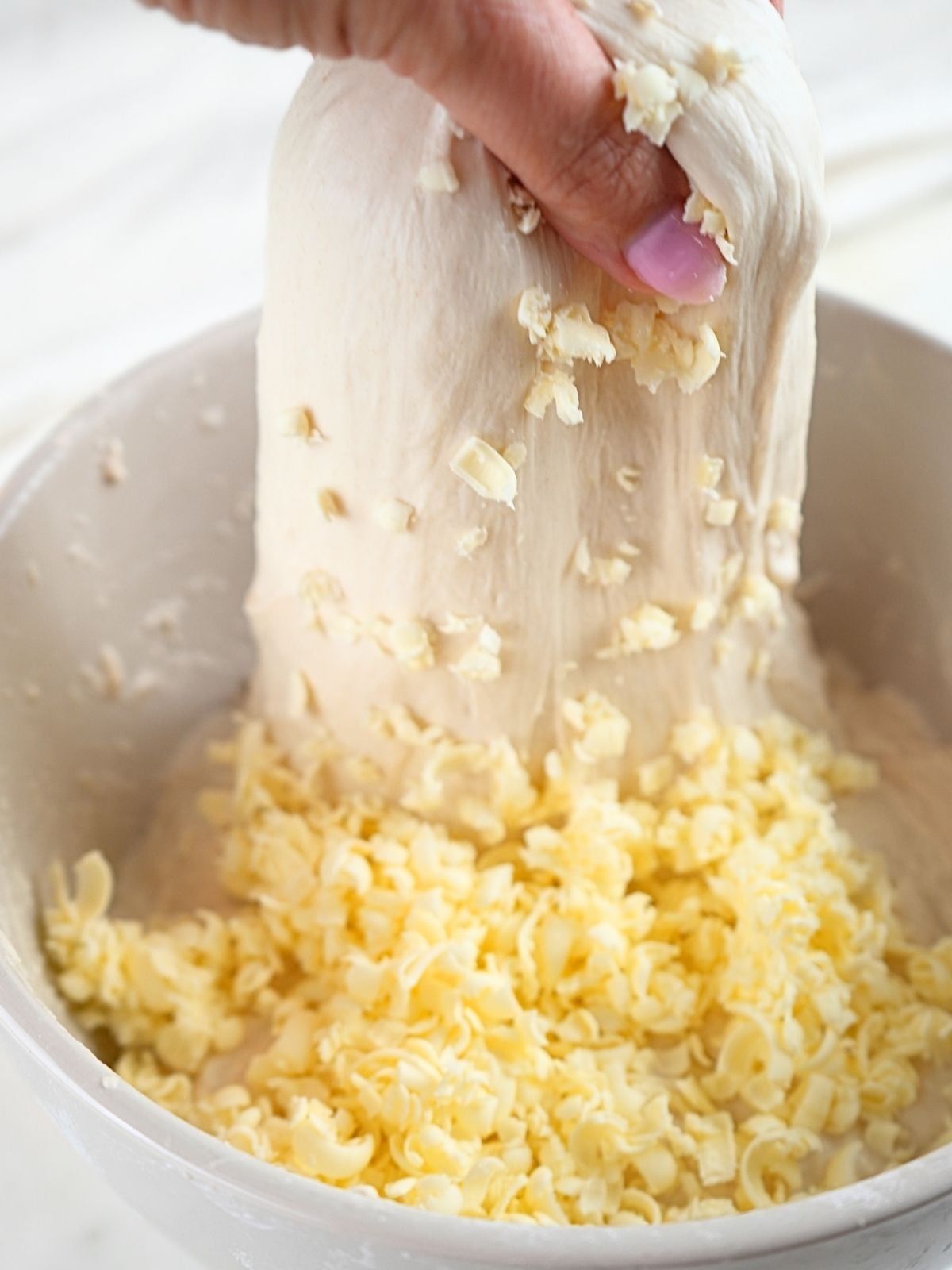 Butter and dough in a bowl with a hand showing stretch and folds.